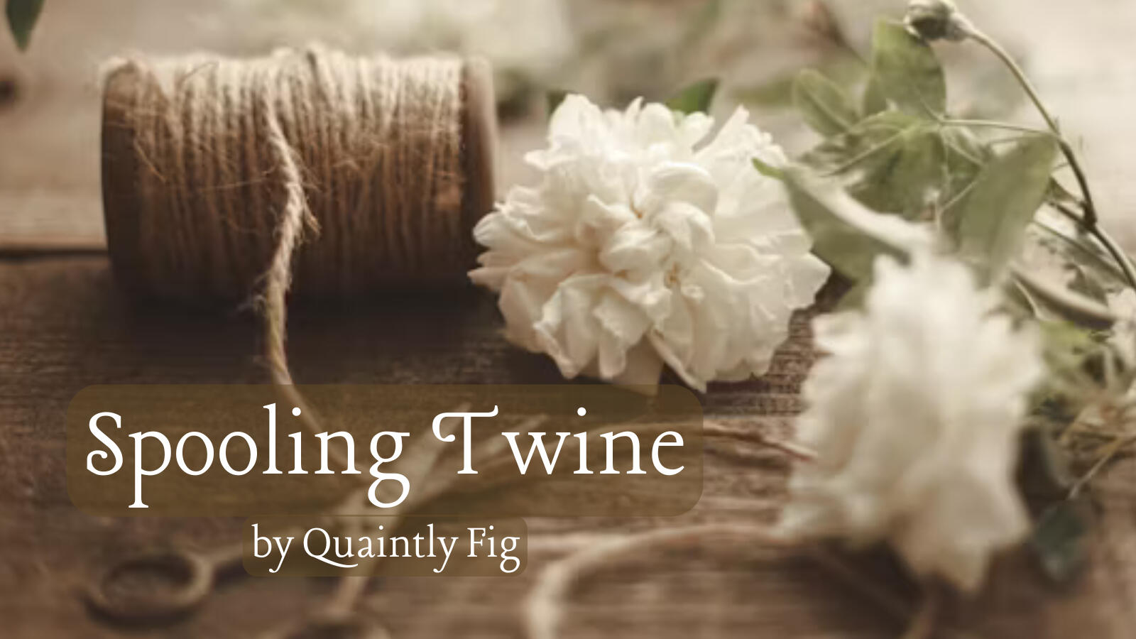 Text: Spooling Twine by Quaintly Fig; Image: A spool of twine lies on its side on a wooden surface next to two white flowers. An out-of-focus pair of scissors sits near the bottom of the image over the thread of twine that is coming off the spool.